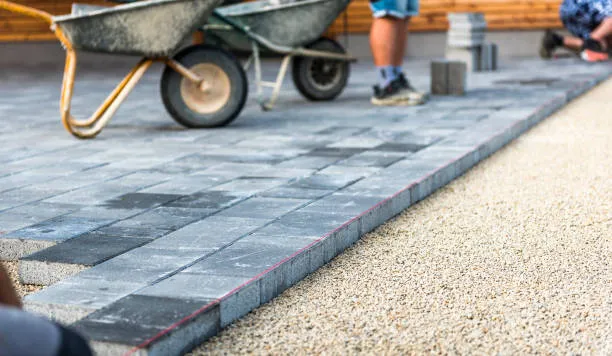 Installers laying interlocking concrete pavers over a prepared base in Austin