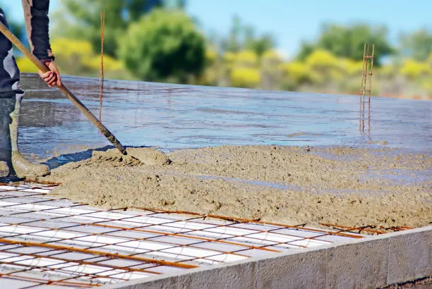 Contractor leveling a freshly poured concrete slab with a screed board